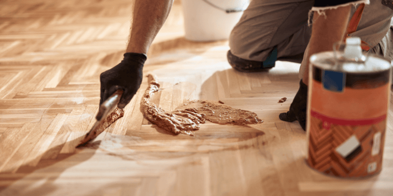 Repairman restoring old parquet hardwood floor with wood grain filler.