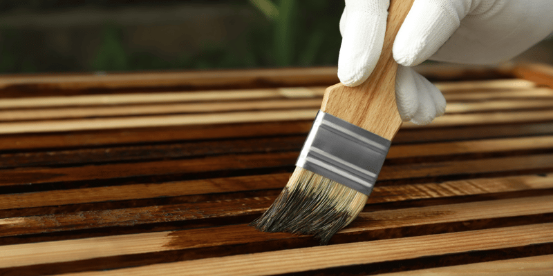 applying wood stain to wooden planks with bristle brush