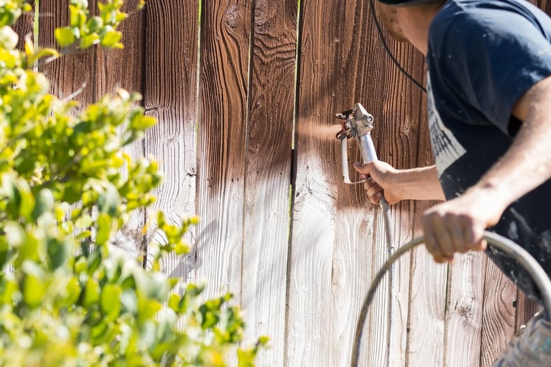 contractor spraying on wood stain to protect yard fence